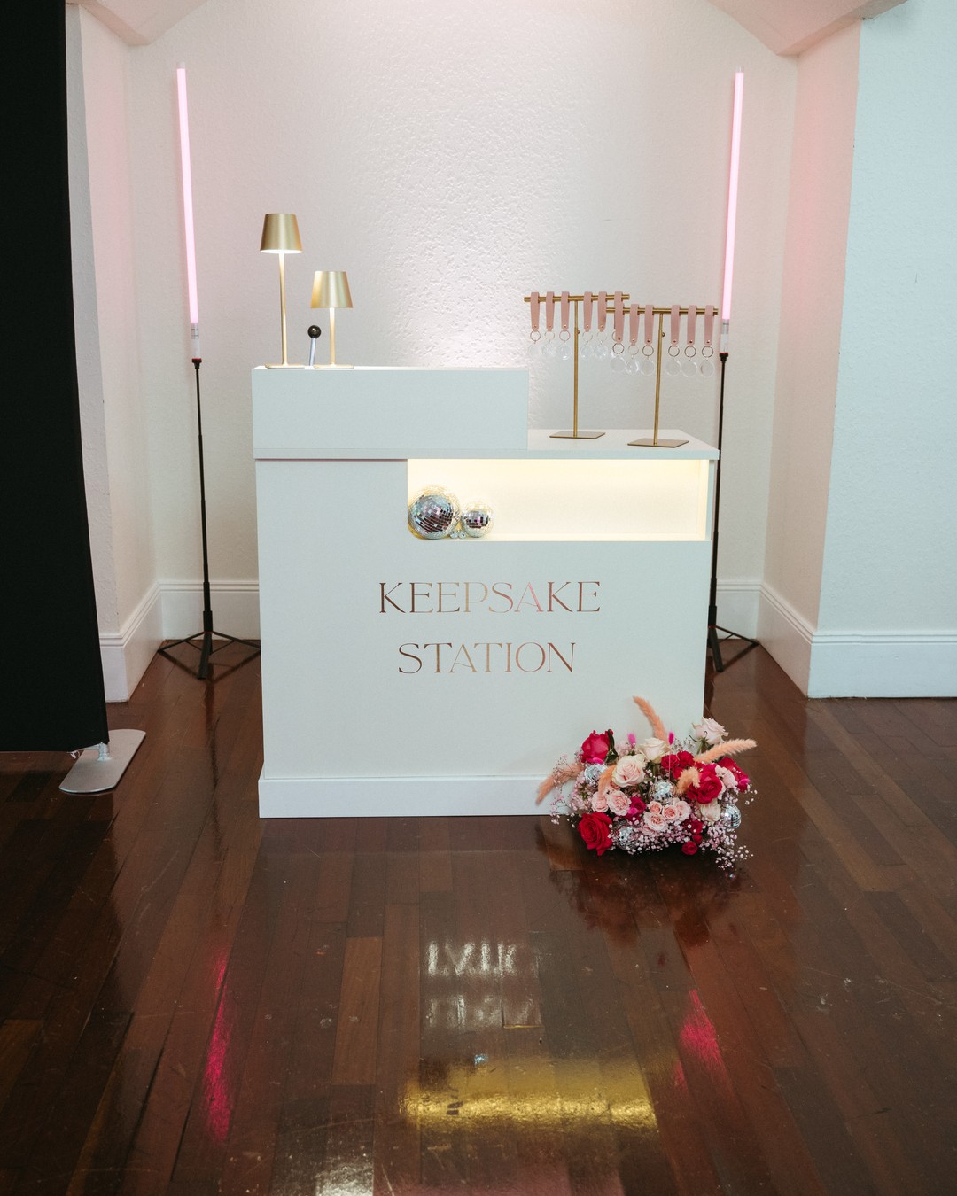 White keepsake bar with gold "Keepsake Station" lettering, gold lamps, pink light columns and flowers